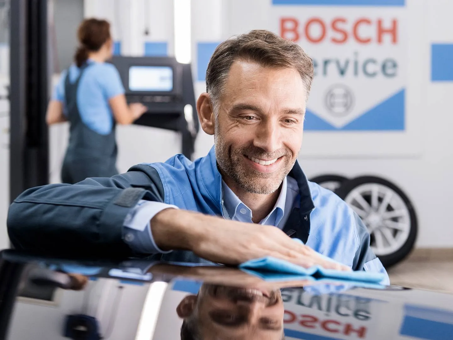 Freundlich lächelnder Mechaniker reinigt ein Auto in einer modernen Werkstatt. Stimmungsvolles Motiv für Servicekampagnen und Markenkommunikation im Automotive-Bereich.