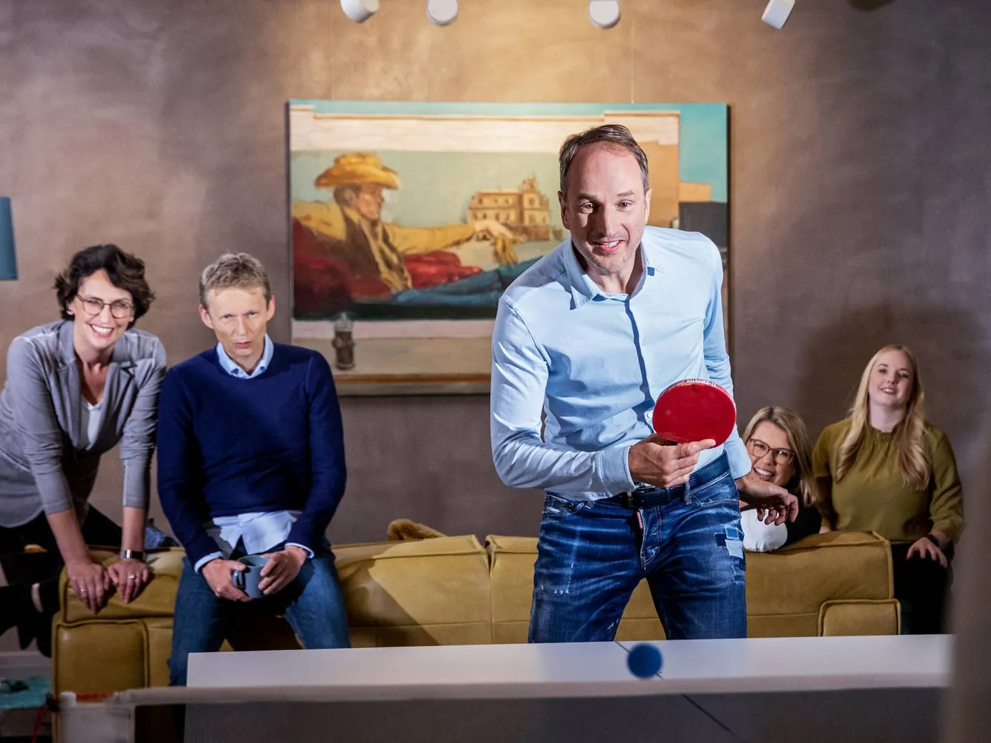 Gruppe von Menschen spielt Tischtennis im Wohnzimmer. Emotionales Motiv für Employer Branding, Teamkommunikation und Markenauftritt mit Persönlichkeit.