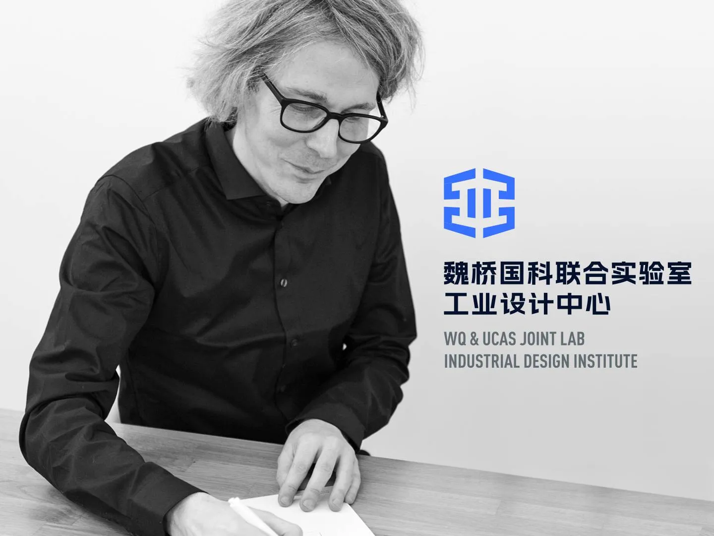 Schwarzweißfoto von Kai Gehrmann an einem Tisch mit Logo. Motiv für internationale Designkooperation, Innovation und Markenkommunikation.