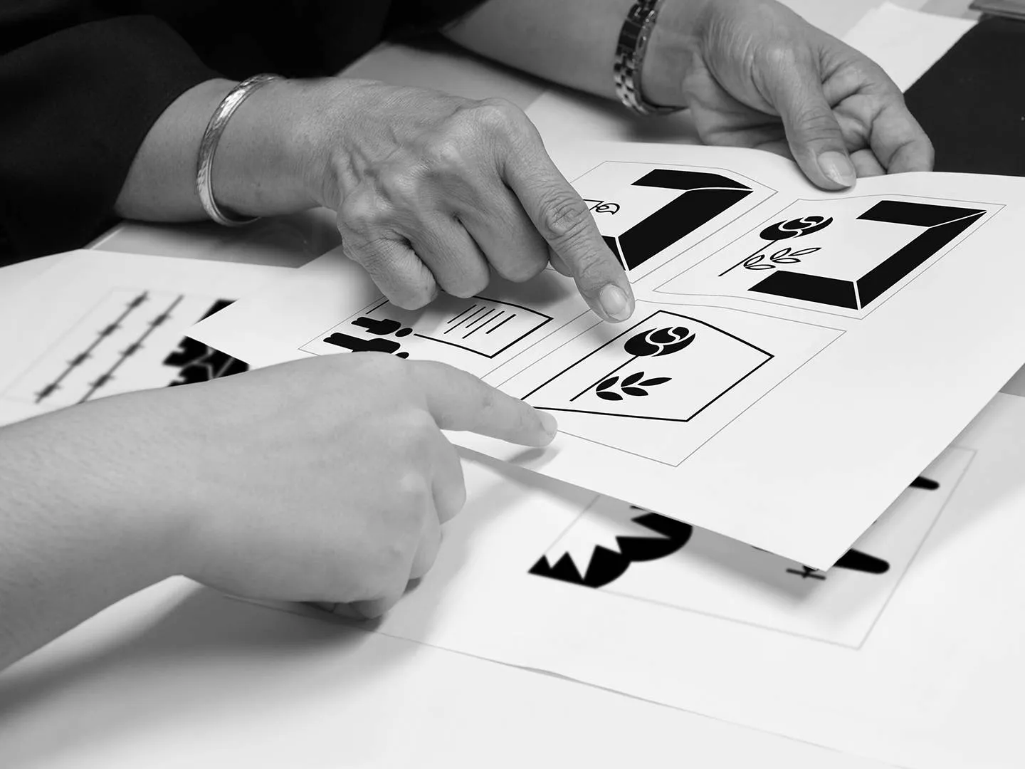 Hände zeigen auf symbolhafte Grafiken in Schwarz-Weiß. Ausdrucksstarkes Motiv für Kommunikationsdesign mit kulturellem und gesellschaftlichem Anspruch.