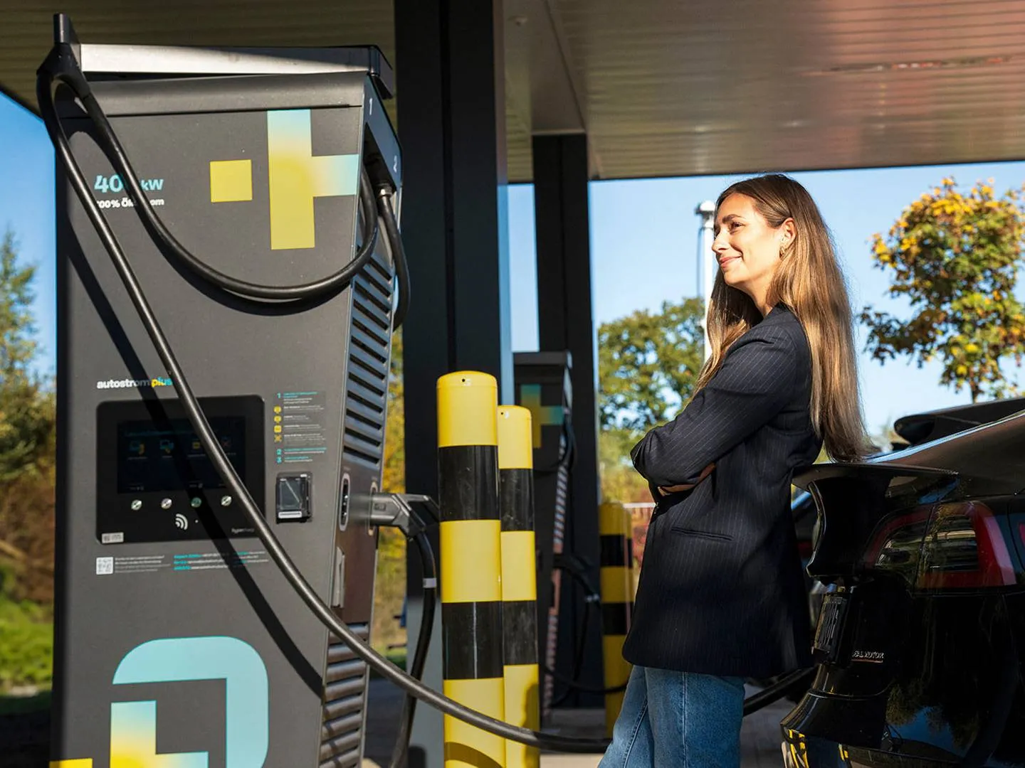Junge Frau lädt ihr E-Auto an moderner Schnellladestation. Stimmungsvolles Motiv für Markenkommunikation rund um Elektromobilität, Zukunft und Nachhaltigkeit.